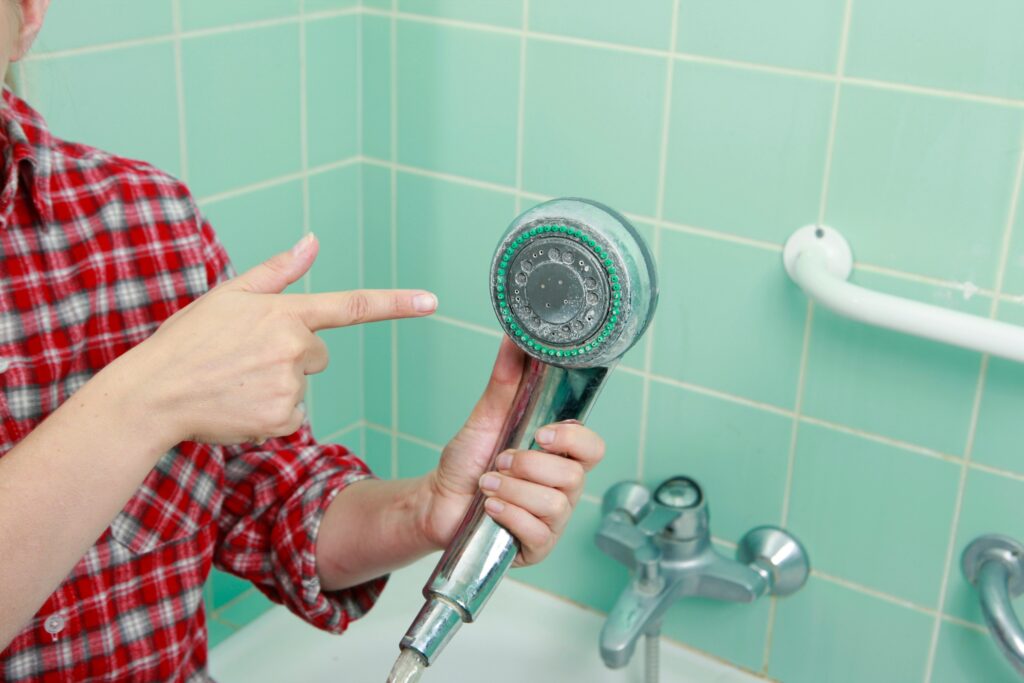 man pointing to shower head with built up mineral depostis